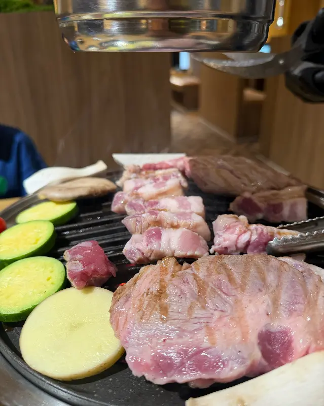 불판 위에서 구워지는 삼겹살과 곁들임 채소