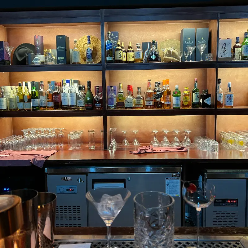 다양한 종류의 술병과 잔들이 진열된 바 테이블의 모습이 보인다.