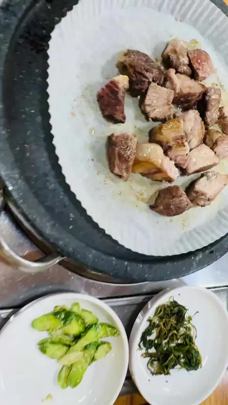 돌판 위에 먹기 좋게 잘려진 흑돼지 구이가 놓여 있고, 곁들임 채소가 함께 보인다.