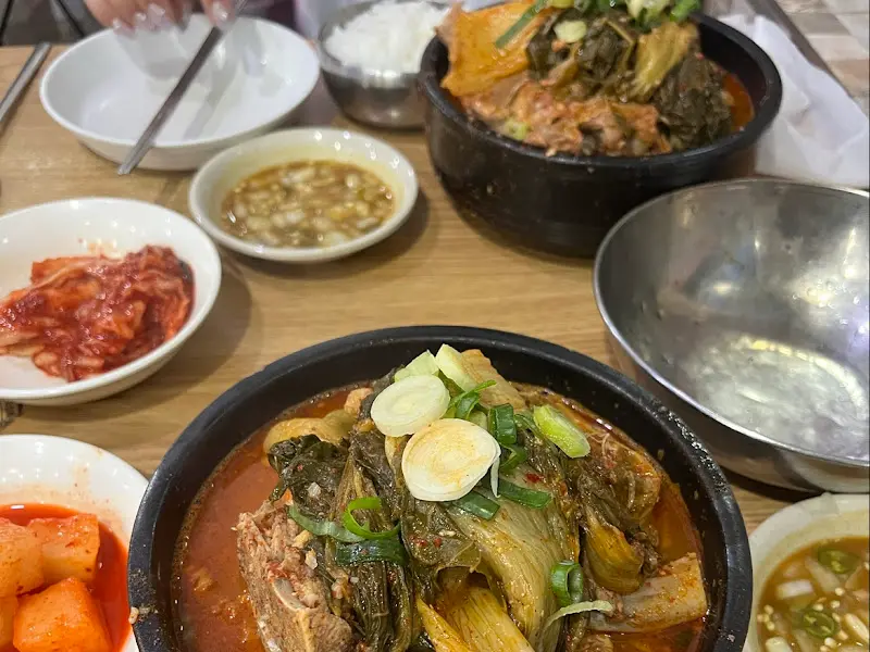테이블 위에는 감자탕이 담긴 냄비와 깍두기, 김치, 밥, 겨자 소스가 놓여 있다.