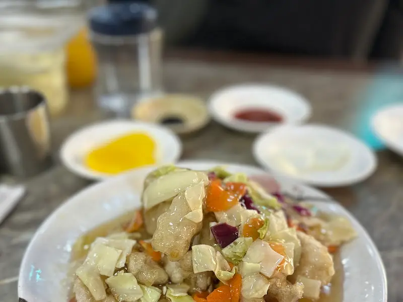 탕수육 위에 소스가 듬뿍 뿌려져 있고, 양배추, 당근, 양파 등 다양한 채소가 함께 올려져 있는 모습