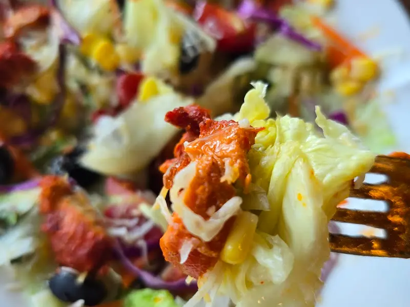 탄두리 치킨이 얹어진 샐러드를 포크로 들어올린 모습