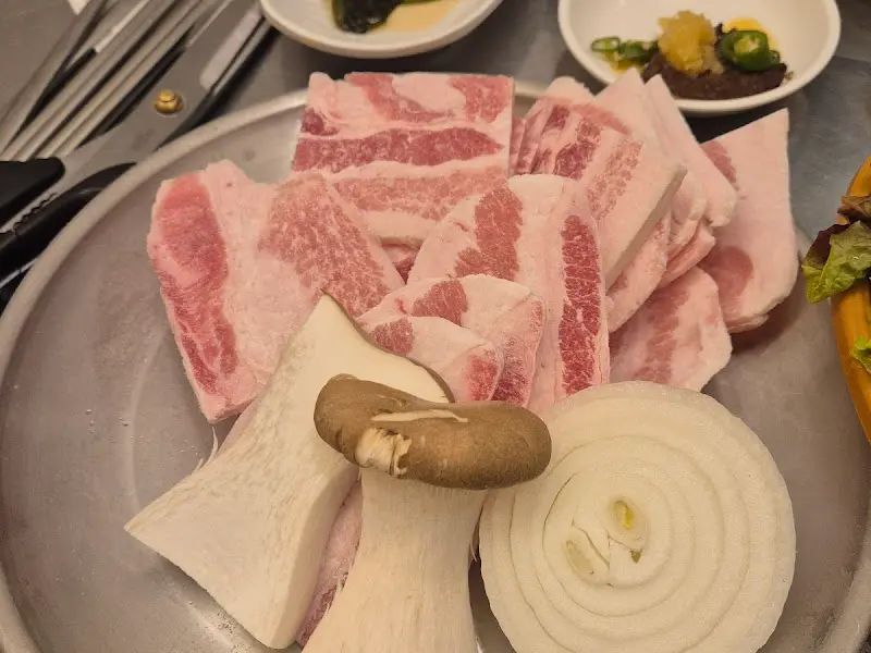 불판 옆에 가지런히 놓인 냉동 삼겹살 접시