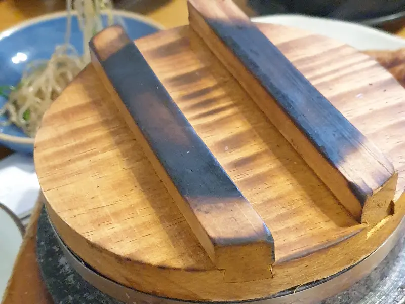 돌솥의 나무 뚜껑이 덮여있는 모습, 뚜껑의 나무 결이 따뜻한 느낌을 준다.