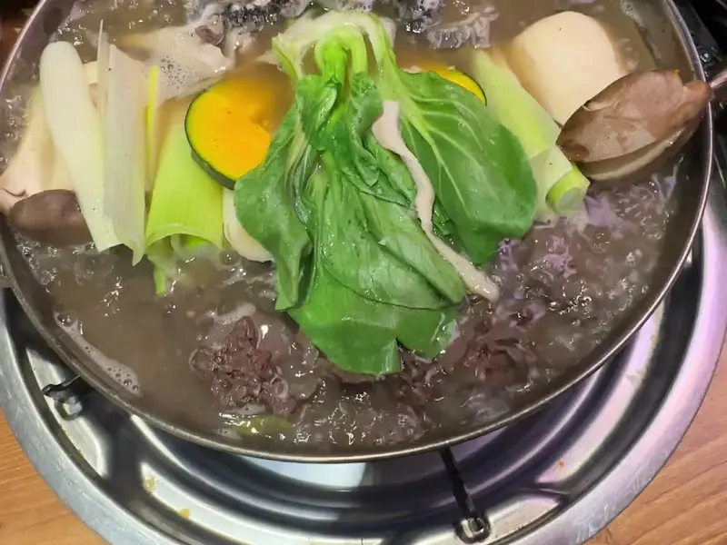 металлический горшок, полный множества ингредиентов, таких как зеленые овощи, тыква и красные куски