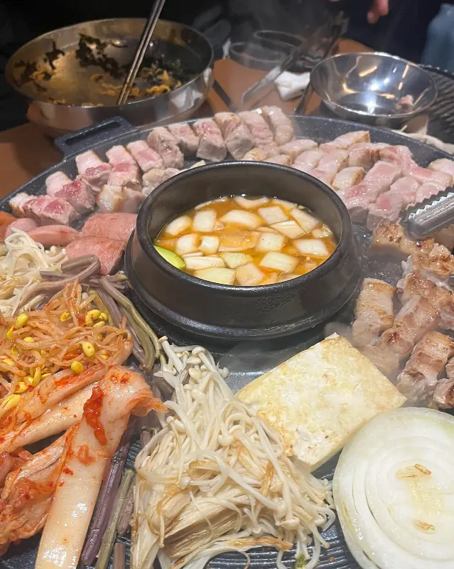 솥뚜껑 가득 차려진 삼겹살과 곁들임 찬들의 모습