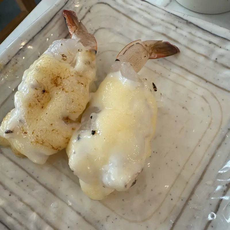 흰색 접시에 담긴 구운 새우 초밥 두 점