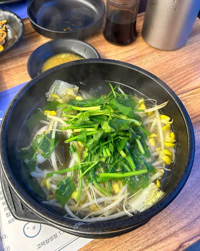 검은색 뚝배기에 담긴 복지리에는 미나리와 콩나물이 가득 들어 있다.