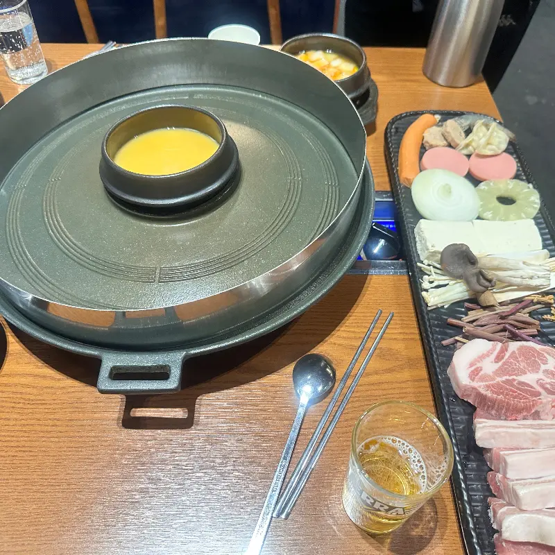 솥뚜껑과 삼겹살, 그리고 곁들임 재료들이 한 상에 놓여 있는 모습