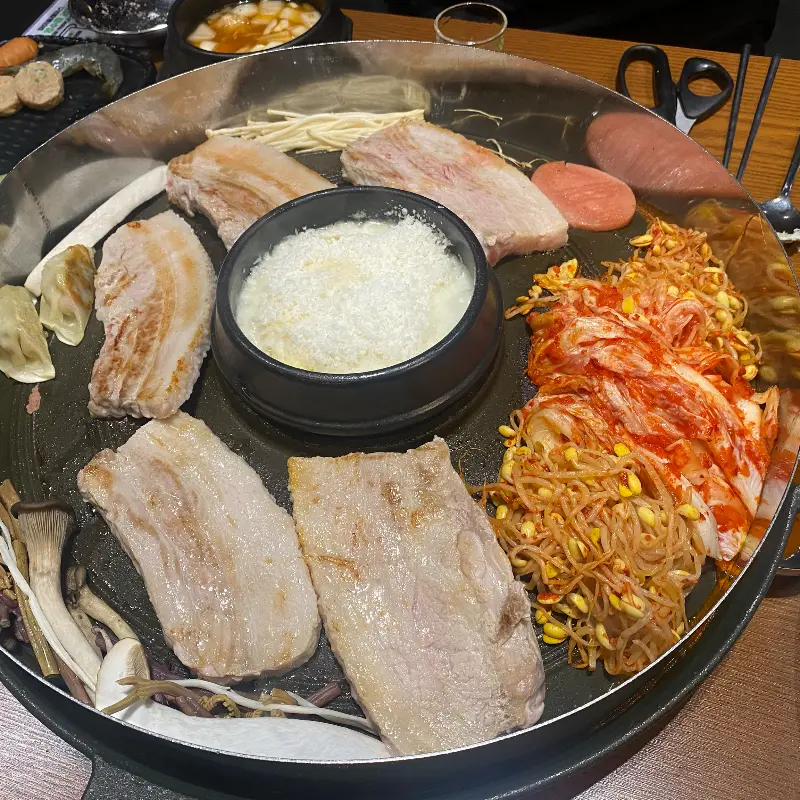 솥뚜껑에 구워진 삼겹살과 김치, 콩나물, 버섯의 조화