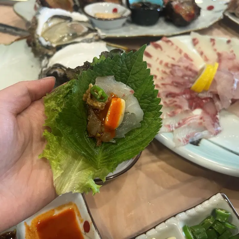 손에 들린 깻잎 쌈 위에 올려진 회 한 점