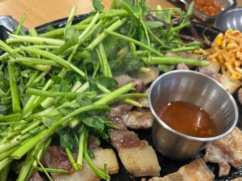 불판 위에 올려진 삼겹살, 미나리, 김치