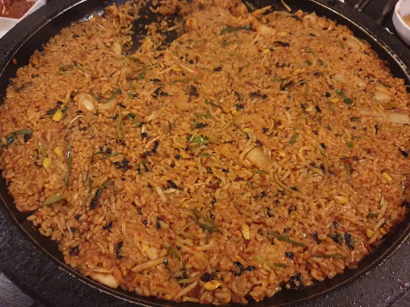 볶음밥이 넓은 불판 위에 펼쳐져 있다. 김가루와 야채가 듬뿍 뿌려져 있다.