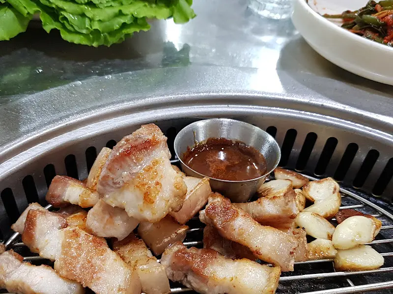 잘 구워진 흑돼지 삼겹살과 구운 마늘이 멜젓과 함께 놓여있는 모습