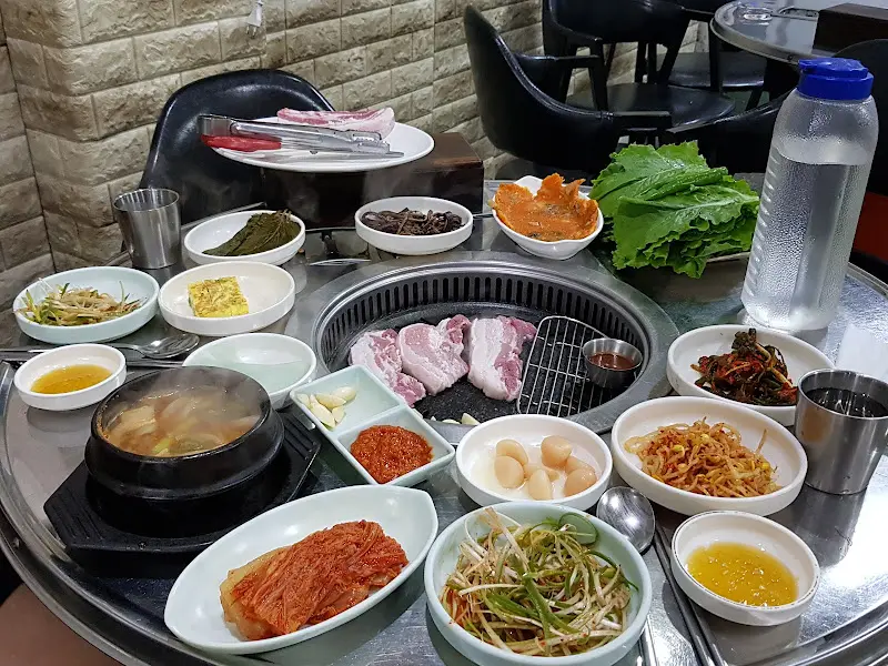 흑돼지 삼겹살 한 상 차림. 다양한 밑반찬과 된장찌개가 함께 놓여있다.