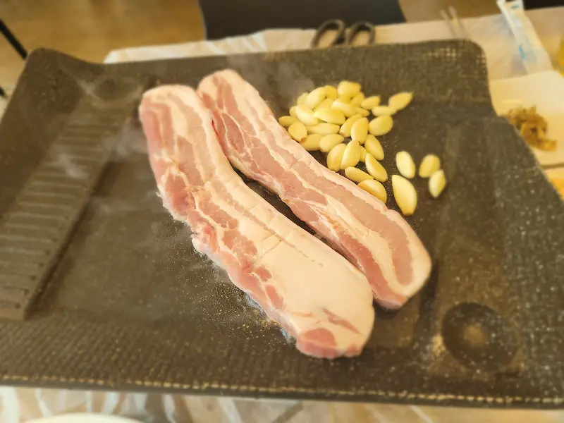 불판 위에서 노릇하게 익어가는 삼겹살과 마늘