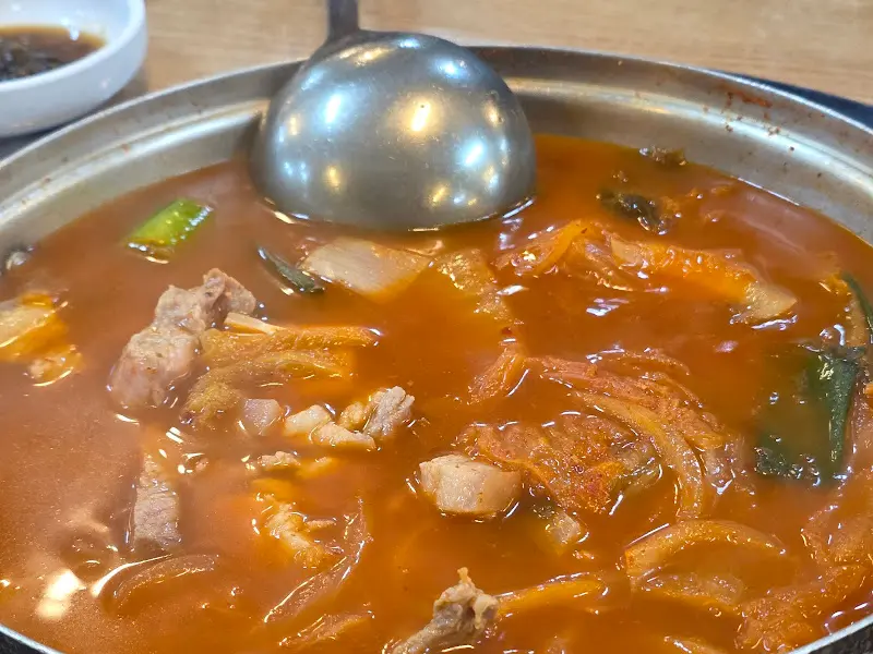 김치찌개의 붉은 국물과 큼지막한 돼지고기가 돋보이는 사진