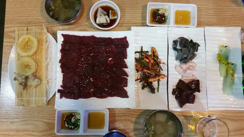 테이블 위에 놓인 뭉티기와 곁들임, 술잔이 함께 있는 정경