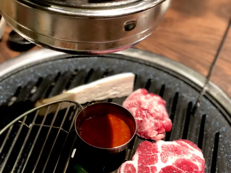 불판 위에서 구워지는 돼지고기와 버섯, 그리고 작은 종지에 담긴 소스의 모습