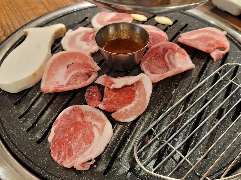 불판 위에 가지런히 놓인 돼지고기와 새송이버섯, 가운데에는 멜젓이 담겨 있다.