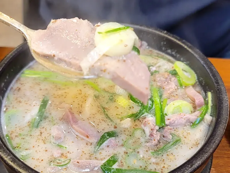 숟가락으로 순대국 안의 내용물을 들어올린 모습. 순대와 고기가 푸짐하게 들어있다.