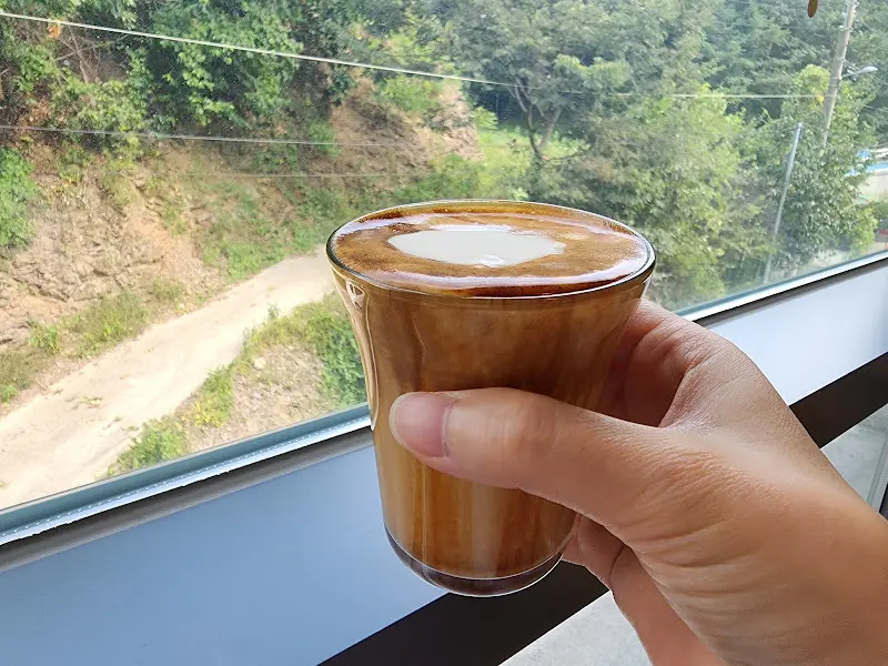 손에 들린 Mallang. 라떼 사진. 창밖의 풍경이 보인다.