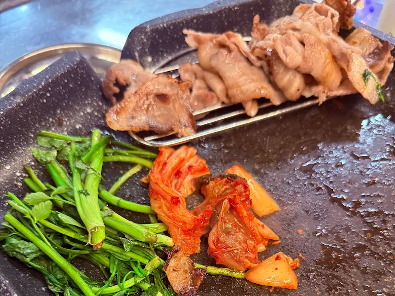 불판 위에서 익어가는 냉삼겹살, 김치, 미나리