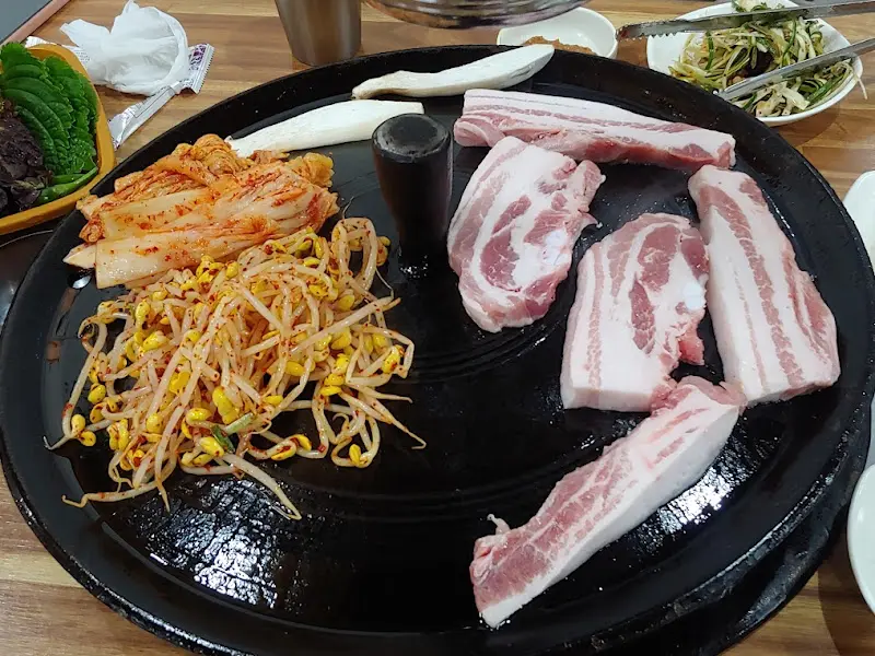 솥뚜껑에 삼겹살과 김치, 콩나물이 함께 구워지는 모습