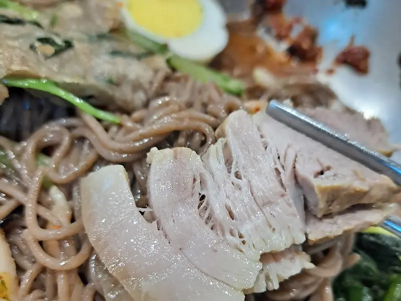 젓가락으로 집은 수육과 메밀면
