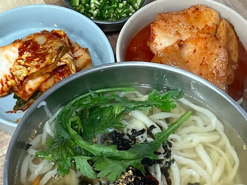 테이블 위에 놓인 칼국수, 김치, 석박지, 다진 고추