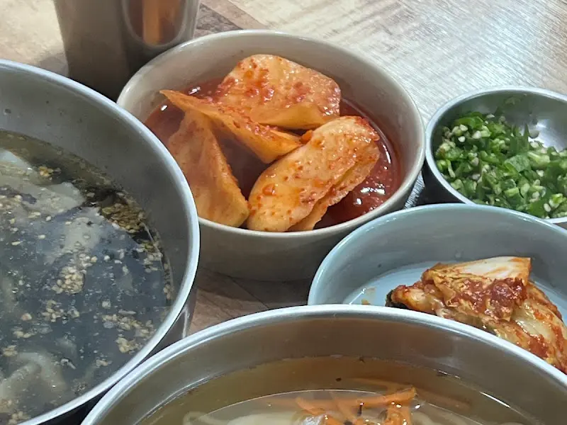 테이블 위에 놓인 칼국수, 김치, 석박지, 다진 고추