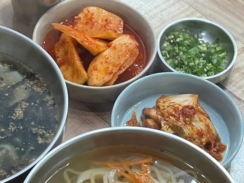 테이블 위에 놓인 칼국수, 김치, 석박지, 다진 고추