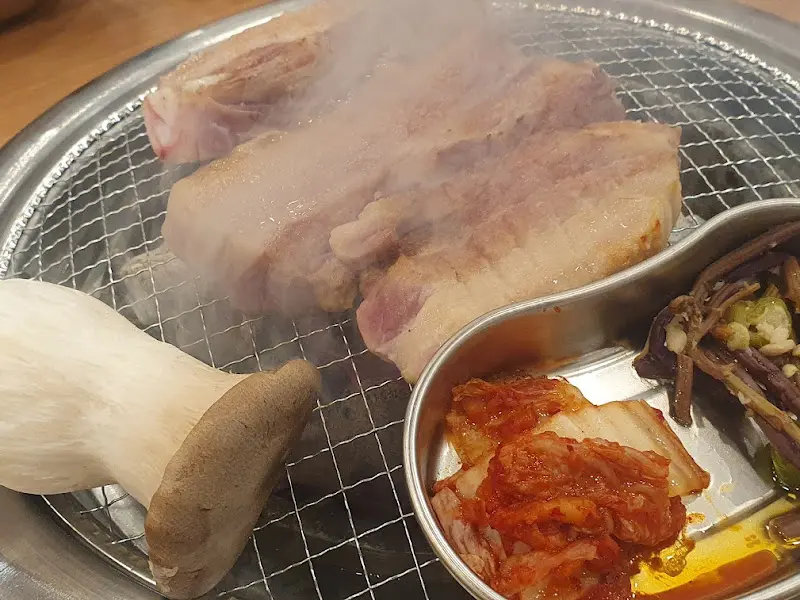 잘 익은 삼겹살과 김치를 솥뚜껑에 함께 구워먹는 모습