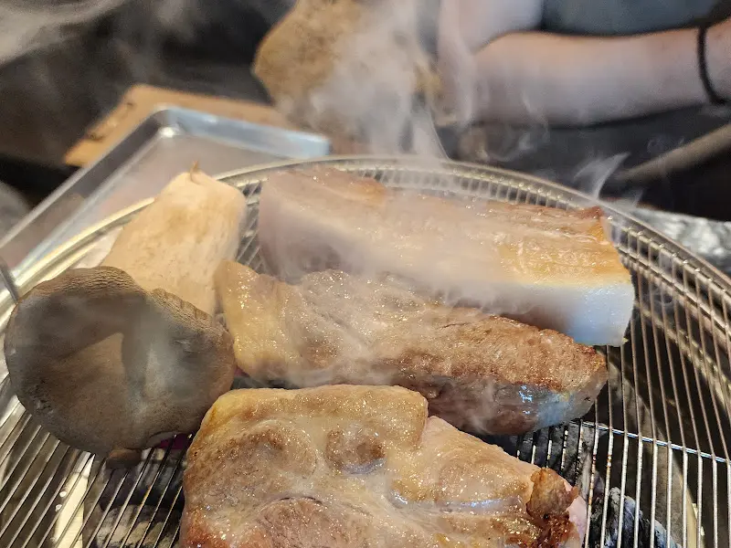 잘 익은 삼겹살과 통통한 새송이버섯이 숯불 위에서 먹음직스럽게 익어간다.