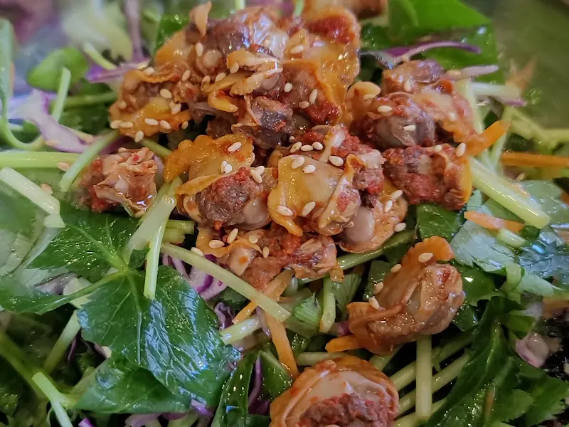 꼬막 무침의 클로즈업 샷, 윤기가 흐르는 꼬막과 깨가 식욕을 자극한다.