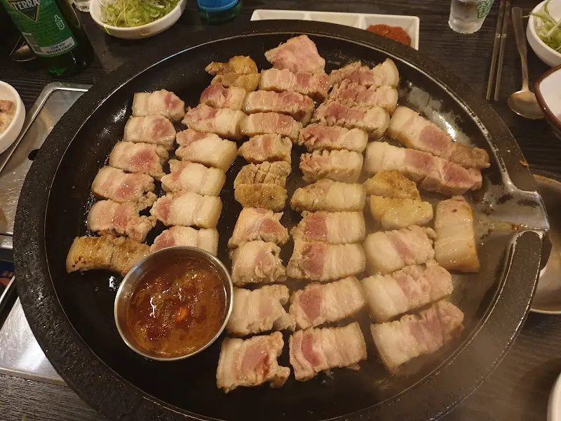 초벌된 두툼한 제주 흑돼지 오겹살이 불판 위에 가지런히 놓여 있다.