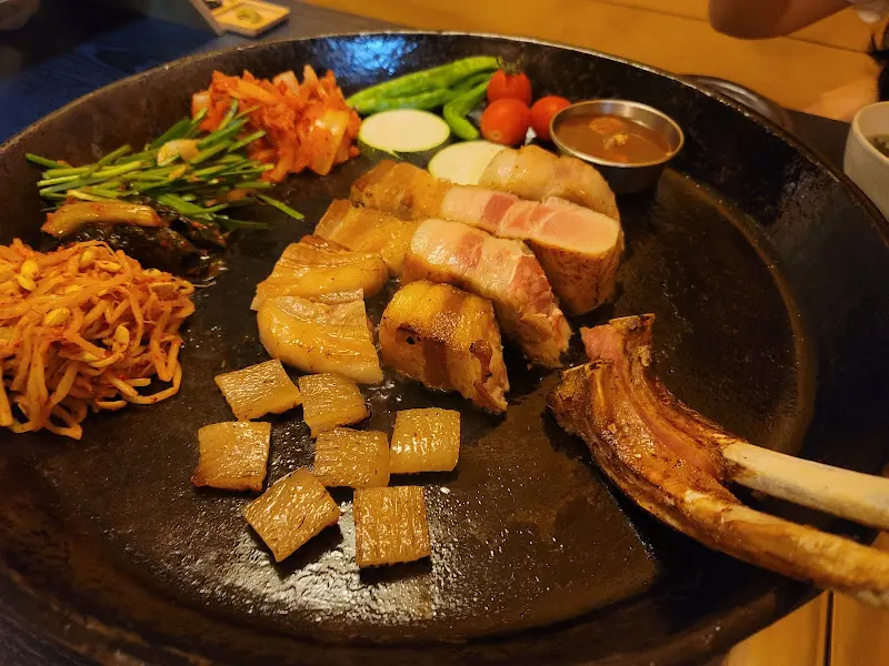 잘 구워진 오겹살과 곁들임 채소들이 불판 위에 함께 놓여 있다.