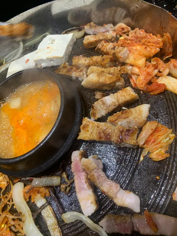 솥뚜껑에 삼겹살, 김치, 콩나물이 함께 구워지는 모습