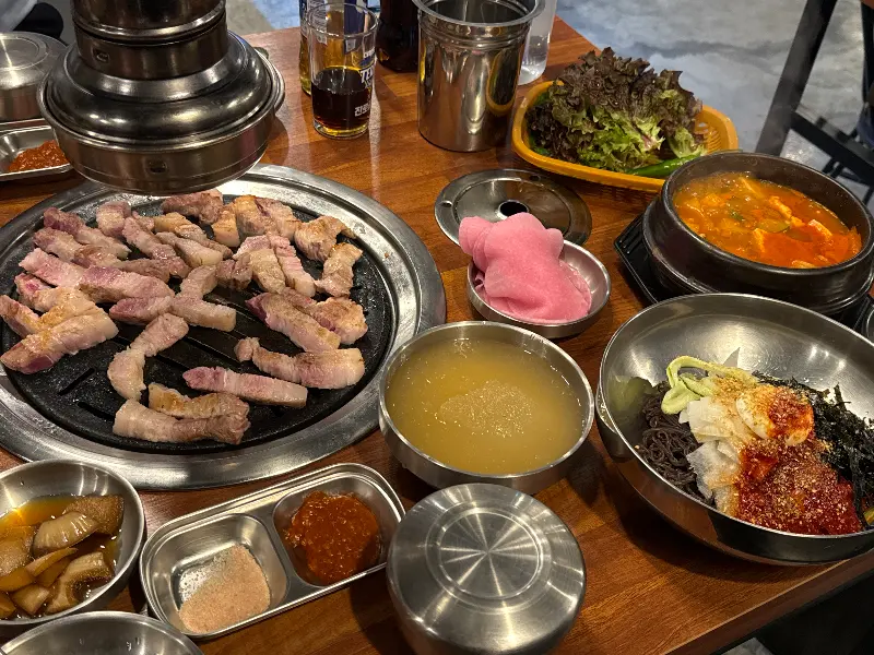 불판 위에서 맛있게 익어가는 삼겹살과 밑반찬