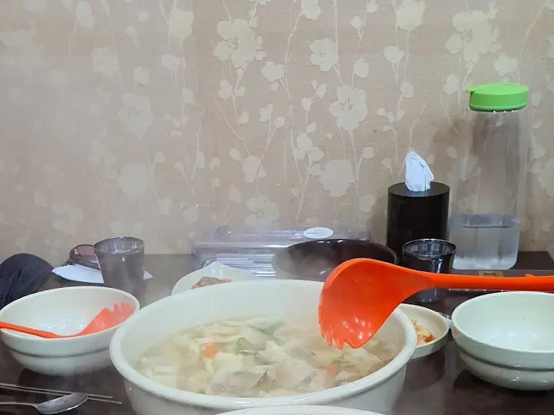 테이블 위에 놓인 해물 칼제비가 담긴 그릇과 국자를 든 손