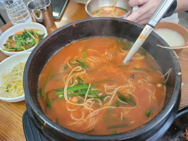 큰 뚝배기 안에는 소면과 수제비 사리가 넉넉하게 들어있고, 국물은 진한 주황색을 띤다.