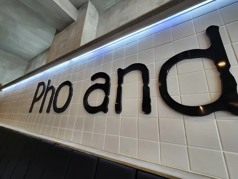 Pho an이라는 검은색 글자가 흰색 타일 벽에 붙어 있다. 위에는 은은한 조명이 비치고 있다.