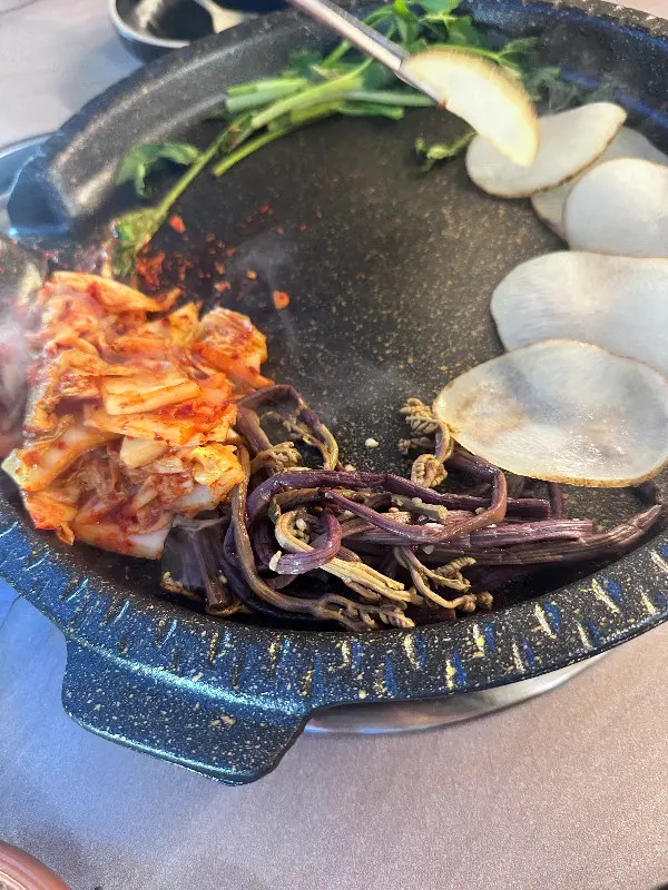 불판 위에서 맛있게 익어가는 김치와 냉동 삼겹살