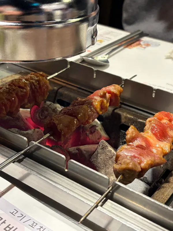 숯불 위에서 노릇하게 구워지고 있는 양꼬치의 클로즈업 샷