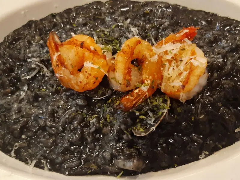 검은색 리조또 위에 새우 세 마리가 올려져 있다.