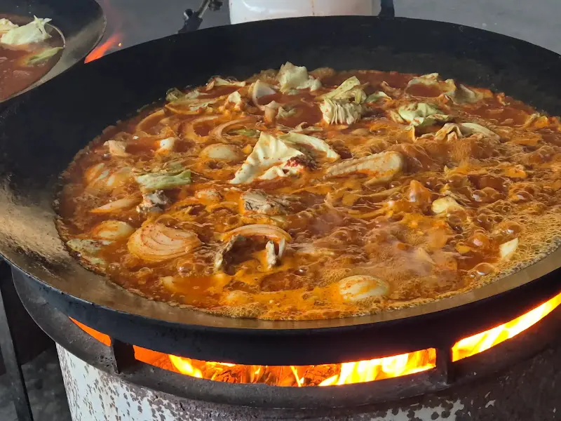 솥뚜껑에 담긴 닭볶음탕이 장작불 위에서 끓고 있는 모습