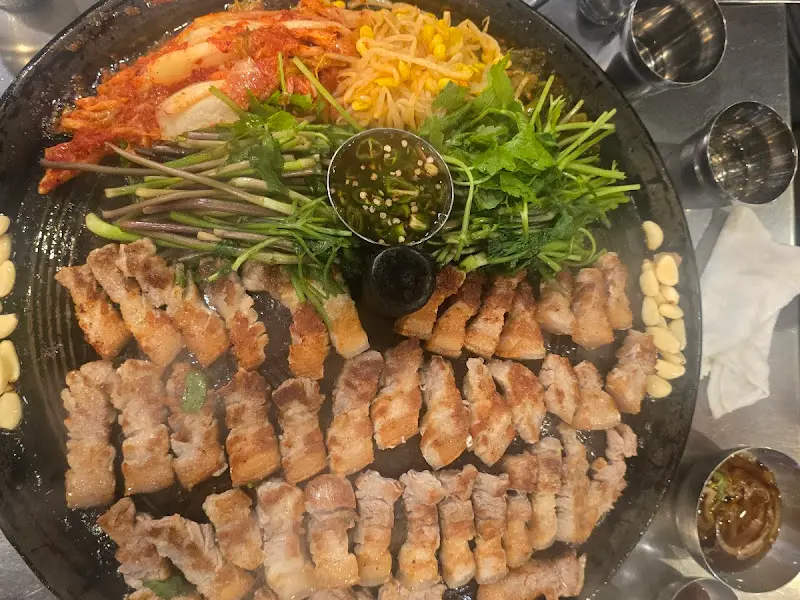 삼겹살, 김치, 콩나물, 마늘이 구워진 솥뚜껑