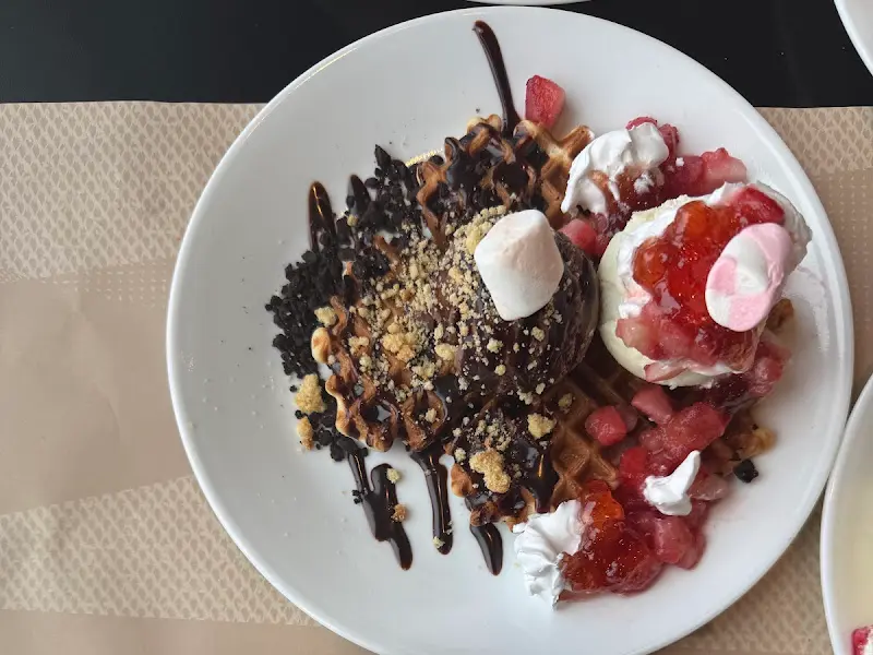 와플 위에 아이스크림, 딸기, 초콜릿 시럽 등을 얹은 디저트 사진