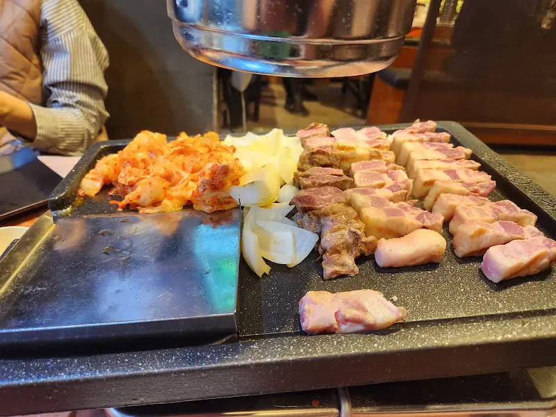 불판 위에 삼겹살, 김치, 양파가 함께 구워지는 모습