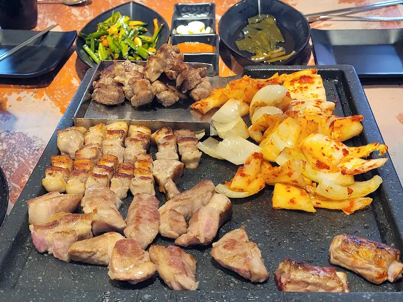 잘 구워진 삼겹살과 다양한 밑반찬들이 함께 놓여있는 테이블